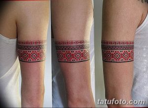 Фото тату: татуировка браслета на руке, выполненная в стиле традиционной народной вышивки. Красные узоры на белом фоне, геометрические мотивы.