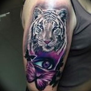 Фото цветной татуировки тигра на руке, украшенной бабочками и изображением глаза. Яркие цвета и детализированный рисунок создают эффектный образ.