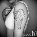 Фото минималистичной татуировки лошади, выполненной в стиле line art на плече. Рисунок состоит из тонких, непрерывных линий, создающих силуэт лошади.