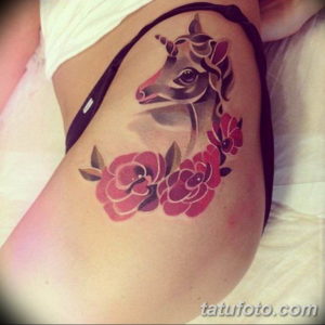 Фото тату на бедре: голова единорога и розовые цветы. Мягкие цвета, грациозный рисунок татуировки, женственный дизайн.