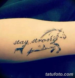 Фотография татуировки с изображением лошади и надписи 'stay strong' на предплечье. Мотивирующий и стильный рисунок.