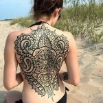 Фото тату: большая черная татуировка в стиле blackwork, имитирующая кружевной узор на спине девушки. Детализированный рисунок татуировки с геометрическими элементами.