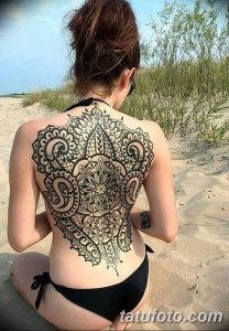 Фото тату: большая черная татуировка в стиле blackwork, имитирующая кружевной узор на спине девушки. Детализированный рисунок татуировки с геометрическими элементами.