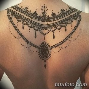 Фото тату: черная татуировка в стиле blackwork, имитирующая кружевной узор на спине девушки. Детализированный рисунок татуировки с геометрическими элементами.