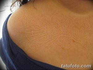 Фото белого тату на плече. Нежный растительный узор с листьями и цветами, выполненный белыми чернилами.