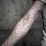 Фото татуировки на предплечье, выполненной в минималистичном стиле с использованием точечного орнамента и черных чернил.