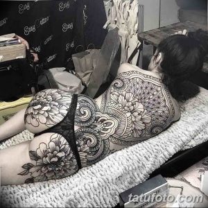 Фотография женского тела, украшенного масштабной татуировкой. Изображены пышные пионы, геометрические узоры и волны, выполненные в черном цвете. Элегантный и сложный рисунок.