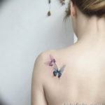 Фото тату с изображением двух акварельных бабочек на женском плече. Нежные переходы цветов и легкий стиль.