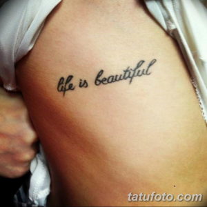 Фото тату: надпись 'Life is beautiful' на плече. Эскиз татуировки выполнен в минималистичном стиле изящным шрифтом.