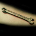 Фото тату реалистичного гаечного ключа John Deere на мужском предплечье. Детализированный рисунок с реалистичными тенями и надписями.