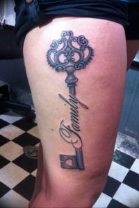 Фото тату большого ключа в серо-черных тонах на бедре, с надписью 'Family'. Реалистичный рисунок татуировки с детальной проработкой.