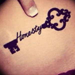 Фото тату на коже: черный ключ с надписью "Honesty". Простая, минималистичная татуировка с четкими линиями.