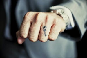 Фото минималистичной татуировки на пальце: маленький ключ, выполненный тонкими черными линиями, символизирующий доступ к чему-то важному.