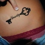 Фото тату на бедре: черный контурный ключ с надписью "Honesty", минималистичный дизайн, изящный рисунок.