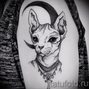 Черно-белое фото тату сфинкса в египетском стиле. Кошка изображена на фоне полумесяца и украшена ожерельем.