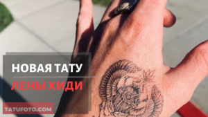 Фотография татуировки скарабея на руке. Черно-белый рисунок с детальной проработкой крыльев и панциря жука. Татуировка выполнена в реалистичном стиле, на фоне рекламного баннера.