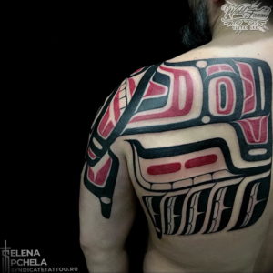 Фото тату на плече: татуировка в стиле Northwest Coast Native с изображением тотемного животного и геометрических узоров. Черно-красный рисунок татуировки.