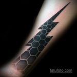Фото тату: стильная черно-серая татуировка в виде молнии, состоящей из гексагональных ячеек, на предплечье.