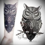 Черно-белое фото татуировки совы в технике blackwork, выполненной на руке. Изображение состоит из плотных черных заливок и геометрических узоров.
