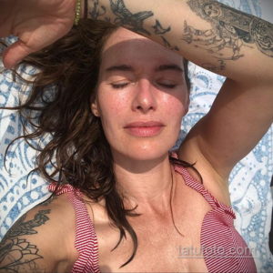 Фотография девушки, лежащей на спине на открытом воздухе, с татуировками на руках, залитых солнечным светом.