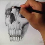Фотография процесса создания эскиза татуировки черепа карандашом, демонстрирующая мастерство художника.