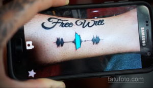 Фото татуировки на предплечье с надписью "Free Will" и изображением волн звука в черном и бирюзовом цветах. Оригинальный рисунок татуировки.