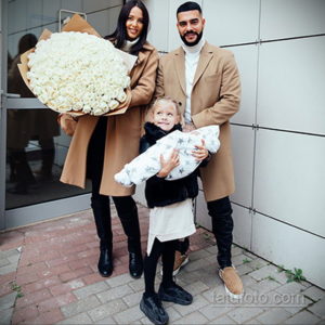 Счастливая пара с дочкой и новорожденным ребенком на руках, держащая большой букет белых роз.