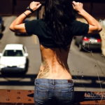 Фото тату: изящная татуировка на спине девушки, изображающая растительные мотивы и плавные линии.