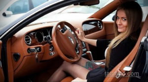 Фото тату: привлекательная девушка за рулем роскошного Bentley, с видимой татуировкой на ноге.