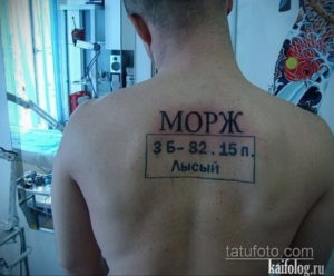 Фото тату: татуировка на спине в виде надписи 'Морж 3 Б-82.15 п. Лысьий', оформленной как штамп. Надпись выполнена черным цветом.