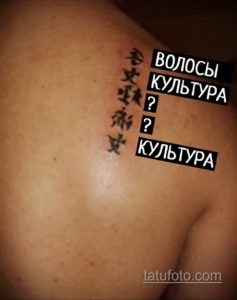 Фото тату на плече с вертикальным рядом китайских иероглифов и надписью 'ВОЛОСЫ КУЛЬТУРА'. Рисунок выполнен в черном цвете, выглядит загадочно и необычно.