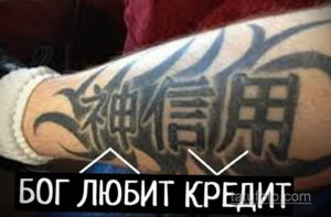 Фото тату на руке с китайскими иероглифами и надписью 'БОГ ЛЮБИТ КРЕДИТ'. Рисунок выполнен в синих и черных тонах, выглядит провокационно и иронично.