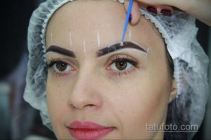 Фото процесса коррекции бровей: мастер наносит разметку на брови девушки в голубой шапочке с помощью синей палочки.