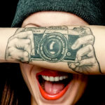 Фото тату на руке: реалистичное изображение камеры Pentax, словно держащейся в руках, черно-белый рисунок.