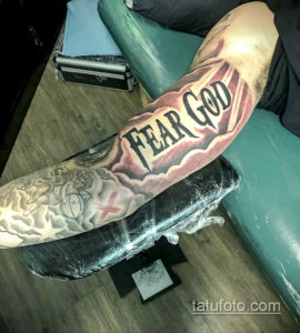 Фото татуировки с надписью 'Fear God' в облаках, выполненной в реалистичном стиле. Религиозный рисунок на руке.