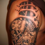 Фото тату: детализированный биомеханический рукав на плече, выполненный в черно-серых тонах с использованием сложных механических элементов и текстур.