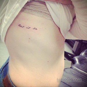 Фото тату с надписью "Let it be" на ребрах, выполненное тонким черным шрифтом. Минималистичный рисунок татуировки, символизирующий принятие и спокойствие.