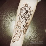 Фото тату на предплечье: ловец снов с символом Инь-Янь в центре, выполненный в технике хенд-поук, с использованием коричневых оттенков.