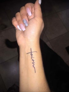 Фото тату: Надпись "Faith" с изображением креста вместо буквы "t" на запястье. Минималистичная и вдохновляющая татуировка.