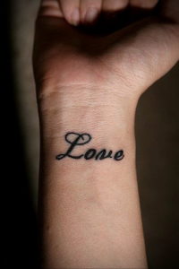 Фото тату надписи 'Love' черным цветом на внутренней стороне запястья. Простой и элегантный рисунок татуировки.