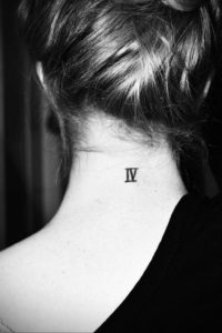 Фото тату: небольшая татуировка с римскими цифрами 'IV' черного цвета, расположенная на задней части шеи девушки.