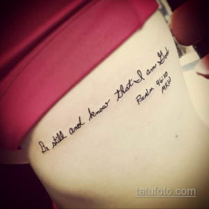 Фото тату с надписью 'Be still and know that I am God' и крестом на спине. Черный контур, каллиграфический шрифт, религиозная символика. Духовная и значимая татуировка.