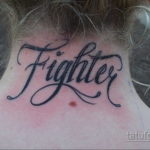 Фото тату с надписью 'Fighter' на шее. Черный контур, каллиграфический шрифт, динамичный дизайн. Татуировка для тех, кто не сдается.