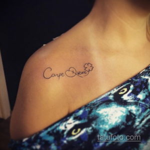 Фото тату с надписью "Carpe Diem" и изображением четырехлистного клевера, выполненной на женском плече.