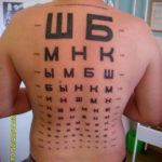 Фото тату на спине: таблица для проверки зрения с буквами разного размера, имитирующая медицинский плакат. Оригинальный и юмористический дизайн.