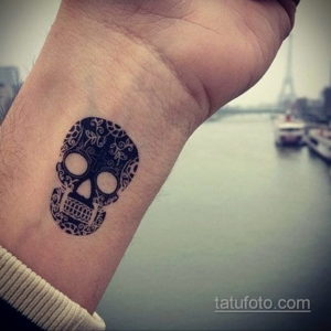 Фото тату черепа в стиле сахарной смерти (calavera) на запястье. Детализированный рисунок татуировки в черном цвете.
