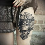 Фото тату лошади в стиле реализм на женском бедре. Детализированный рисунок головы лошади с цветами, выполненный в черно-серых тонах.