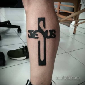 Фото татуировки на ноге: черный крест с надписью 'Jesus', выполненный в минималистичном стиле. Религиозный символ.