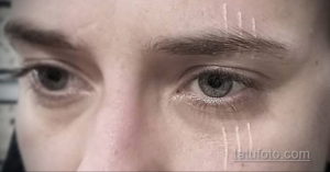 Фотография белой татуировки в виде нескольких вертикальных линий возле глаза. Необычное и смелое решение для тех, кто ценит минимализм.