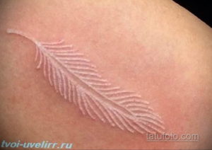 Фотография белой татуировки в виде пера на плече. Рисунок выполнен в технике white ink tattoo и выглядит очень нежно и изящно.